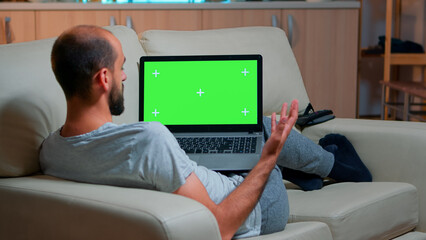 Focused man looking laptop computer with at mock up green screen chroma key display while laying on...