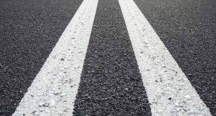 Close view of two solid white road lines on newly laid asphalt surface
