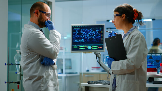 Team of chemists working with DNA scan image looking at desktop standing in medical research laboratory, analysing biochemicals samples, talking. Microbiology development with advanced equipment