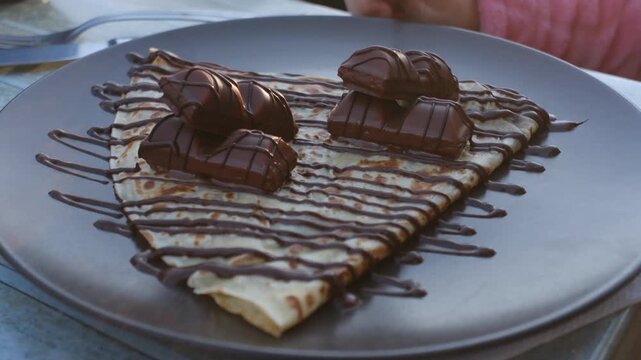 Close-up of a delectable crepe topped with chocolate bars and drizzled syrup.