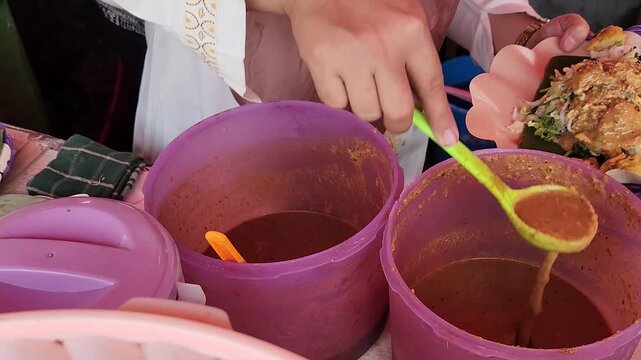 Serving delicious pecel with savory peanut sauce by street vendor. Vendor prepares Indonesian pecel with fresh vegetables and sauce. Pecel, Indonesian salad, with authentic peanut sauce served fresh. 