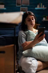 Obraz premium Desperate woman with anxiety problems using mobile phone to browse internet online on living room floor. Sad depressed person with negativity and mental illness difficulties in solitude.