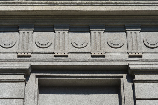 Detailed view of a grey textured building facade featuring classical relief ornaments with vertical lines and circular shapes