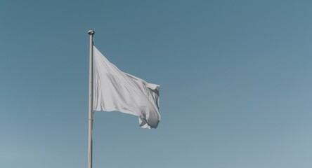 A white flag unfurls gracefully above a flagpole against a clear sky backdrop