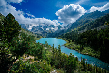 Naklejka premium Alpine lake with snow-capped mountains and lush greenery under blue sky