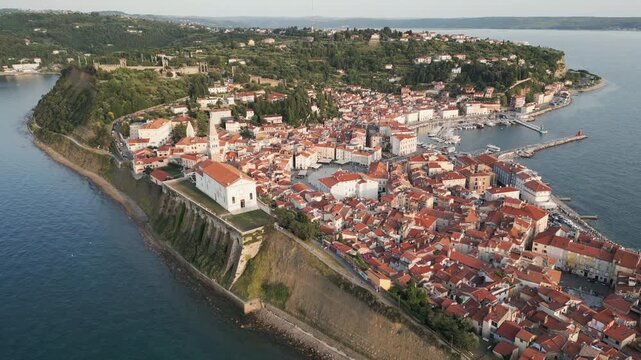 Drone flying towards the historic old town of Piran, an Adriatic coastal gem located in southern Slovenia. Golden hour, natural light.