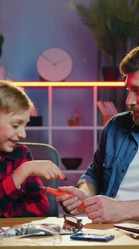 Portrait of likable positive loving 35-aged dad which having fun together with his joyful 12-aged son during funny game with small screwdriwers like as swords while attaching parts to electronic board
