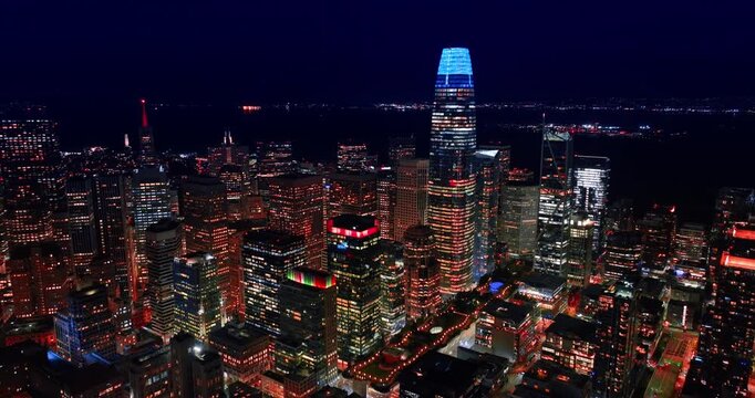 Flying towards the Salesforce Tower with neon light at the top at night. Panorama of downtown San Francisco, California, USA from drone.