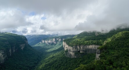 Obraz premium Cloud filled sky over rich velvet green mountainous landscape including deep forest and prominent gray cliffs