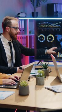 Good-looking purposeful persistent professional male and female office workers sitting around discussing table in modern workroom with night lightings and get aquainted with world statistis datas on