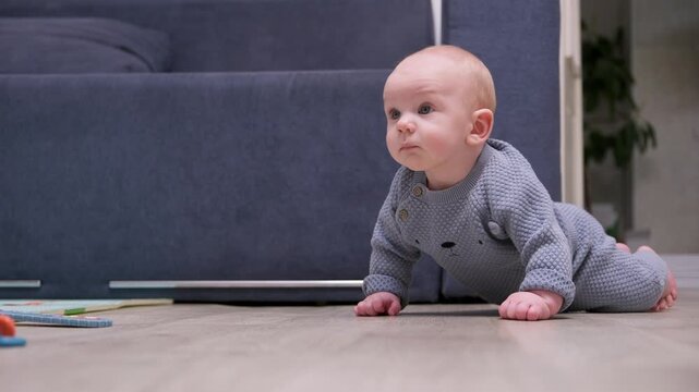 Cute baby with blue eyes learning to crawl on the floor in the living room, exploring the world for the first time. Adorable toddler in grey clothes moving towards his goal