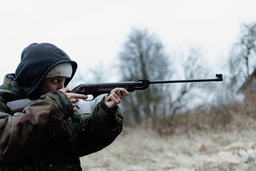 Fototapeta premium A male hunter with a gun in a camouflage jacket in a field in cold weather