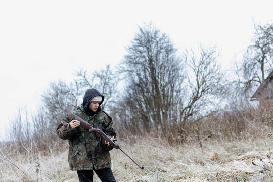 A male hunter with a gun in a camouflage jacket in a field in cold weather