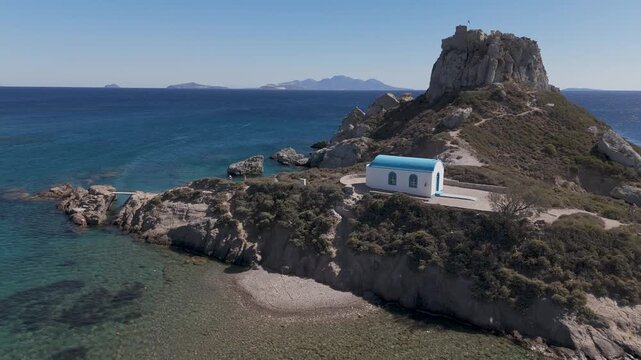 Drone aerial view of white and blue small church in an island in front of Agios Stefanos Beach in Kos Greece