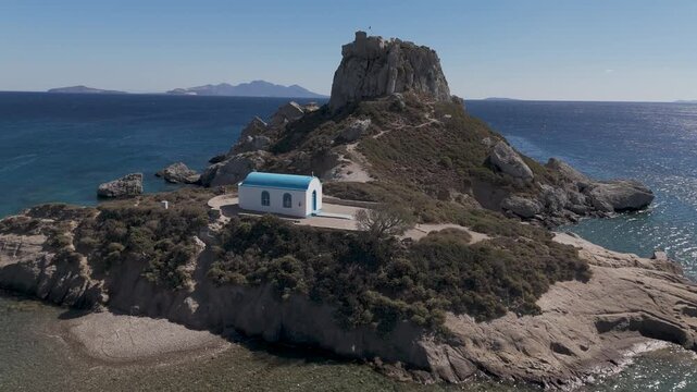 Drone aerial view of white and blue small church in an island in front of Agios Stefanos Beach in Kos Greece