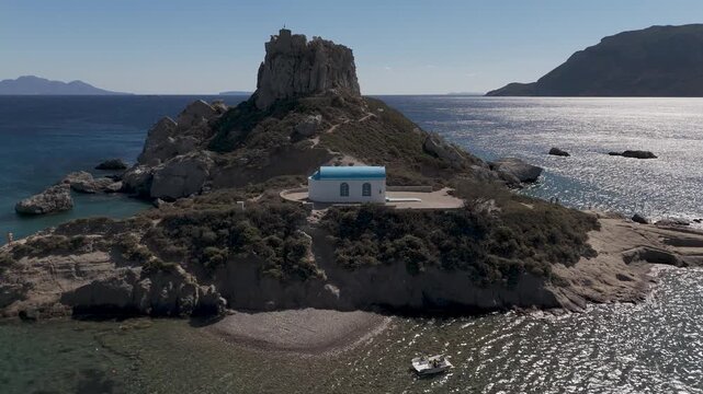 Drone aerial view of white and blue small church in an island in front of Agios Stefanos Beach in Kos Greece