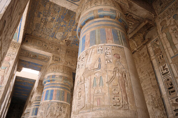 Naklejka premium Low-angle view of massive stone columns inside ancient Egyptian temple decorated with carved hieroglyphs and painted reliefs. Medinet Habu, Theban Hills, West Bank of the River Nile, Luxor, Egypt