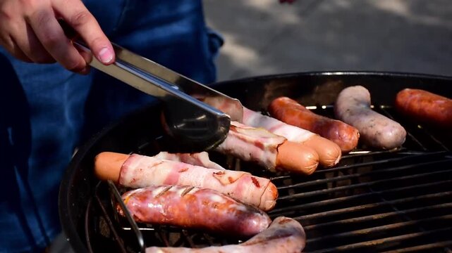 Close up of grilling delicious sausages and bacon wrapped hot dogs on a charcoal grill during a summer backyard barbecue party for outdoor food and family leisure lifestyle.