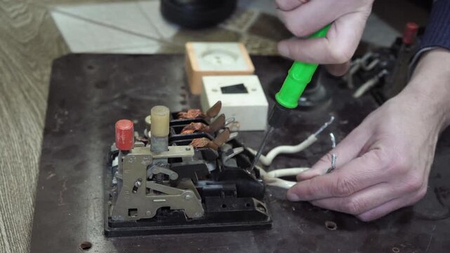 The process of disassembling a three-phase circuit breaker, An electrician works with a screwdriver with terminals of an old circuit breaker