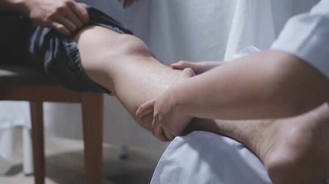 Doctor physiotherapist working examining treating injured knee of patient, his using the handle to the patient knee to check for pain.