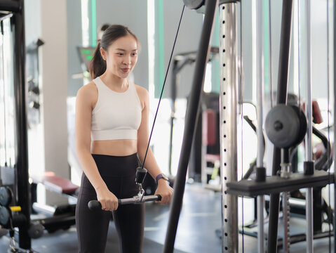 A fit Asian woman is working out with strength training ropes in a gym. Muscle-building workouts at the gym, fitness club, indoor exercise with sports equipment.
