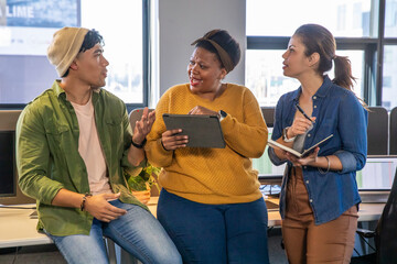 Diverse coworkers collaborating in open-plan office using tablet notebook and gesturing by monitors
