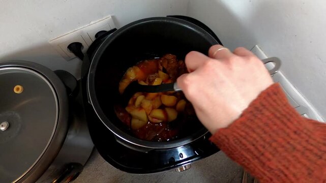 POV view of hands moving meat in sauce with potatoes in an electric pressure cooker.