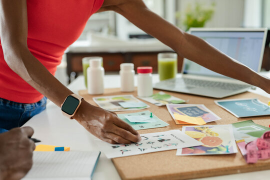 Prints and swatches are being arranged on corkboard on counter near laptop and smoothie