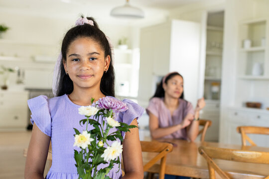 Youth female offering bouquet to mother in kitchen, activating animated floral labels for marketing
