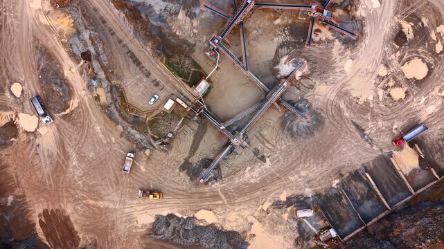 Construction site in active operation. Trucks and machinery work on a construction site with large equipment and piles of material at midday.