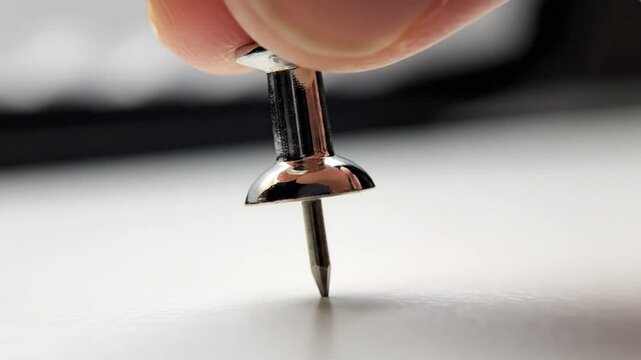 Close up view of a silver push pin standing upright on a white reflective surface demonstrating an object's stillness and stability