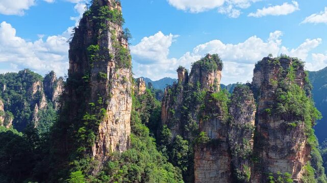 Majestic sandstone pillars rising from lush green forest under blue sky in Zhangjiajie, Hunan, China.