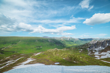 Scenic view from top to multi-tiered dale with melting snows and streams of melt water under lush clouds in blue sky. Colorful landscape with green wide valley. Changeable weather in high mountains. © Daniil