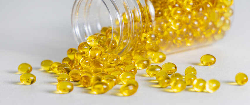 Yellow softgel capsules poured out from transparent bottle on beige stone, healthcare and nutrition