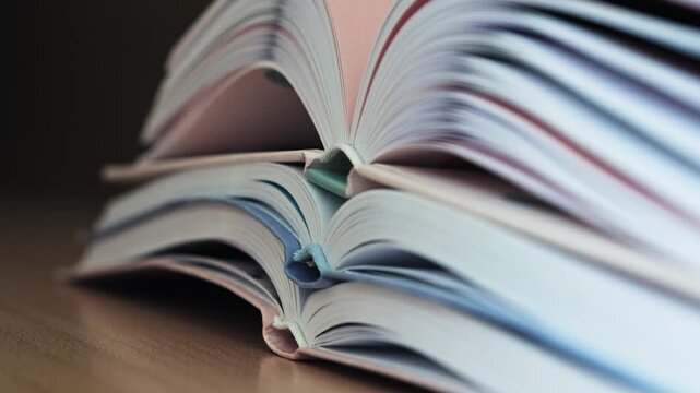 Close up of a stack of open hardcover books lying on a desk with flexible pages rising and gently waving, symbolizing growing knowledge and learning