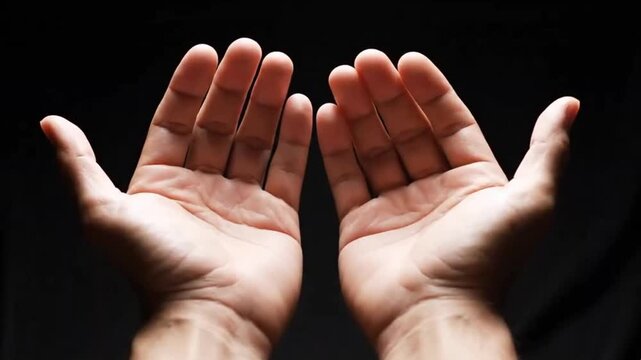 A powerful close-up shot showcases two open human hands, palms facing upwards and slightly cupped, set against a deep, dark, and undefined background. The intentional lighting dramatically highlights 
