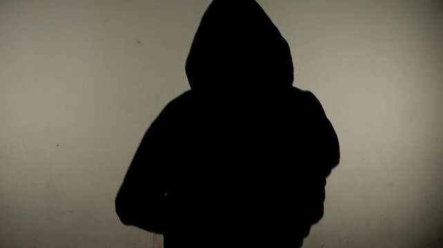 A silhouette of a man in a sweatshirt running towards the camera, against a wall