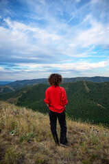 Fototapeta premium A girl in a red shirt on top of a mountain looks into the distance.