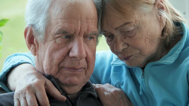 Senior couple cuddles. Older spouses hold each other lovingly inside. Aged married pair affectionately hug in cozy home. Elderly married couple shares experiencing sadness and longing from loss