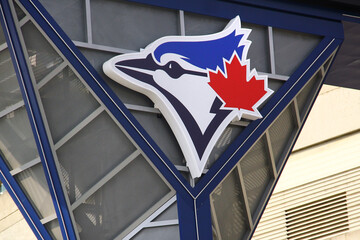 Naklejka premium Toronto, Canada - February 15, 2026: Toronto Blue Jays logo with blue jay and red maple leaf mounted on Rogers Centre stadium facade in downtown Toronto