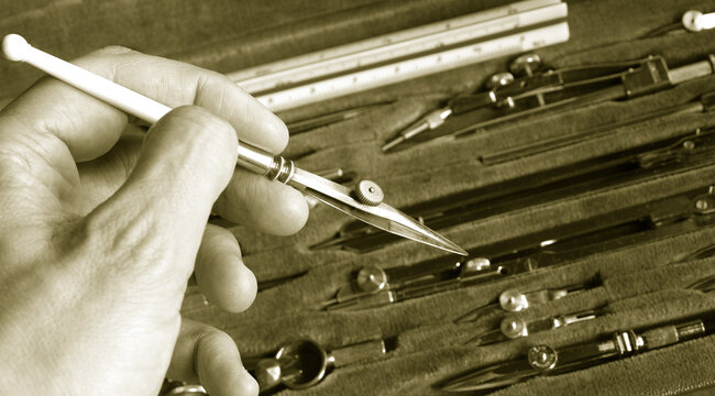 hand with a pen ruler over vintage drafting set