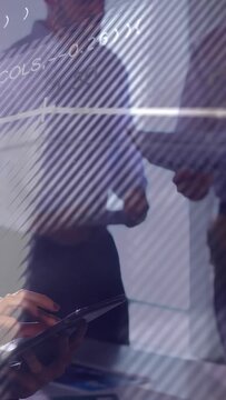 Vertical video: Woman tapping tablet and causing tech overlay on glass while team checking graphs