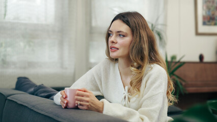 Obraz premium Woman relaxing at home and enjoying a day off. Holding a mug of coffee and sitting on a comfy sofa in the living room