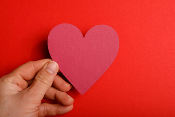 Close up of a hand holding a red heart cutout against a vibrant red background. Perfect for...