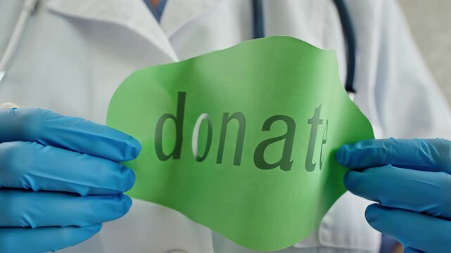 The doctor's gloved hands hold a paper sign with the inscription Donat

