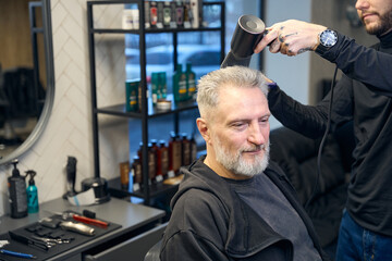 Obraz premium Professional barber using blow dryer styling hair of male client