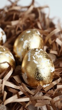 Ornate golden eggs resting in a nest of brown shredded paper inside a simple cardboard carton, for an Easter celebration