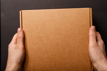 Obraz premium Close-up of hands holding a blank brown cardboard box, perfect for delivery, shipping, or packaging themes.