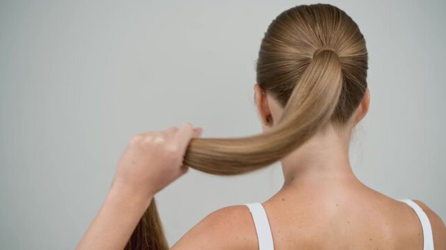 Blonde woman pulling and releasing braid in slow motion, back view close up