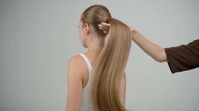 Stylist hand creating waves on thick blonde braid in slow motion, back view